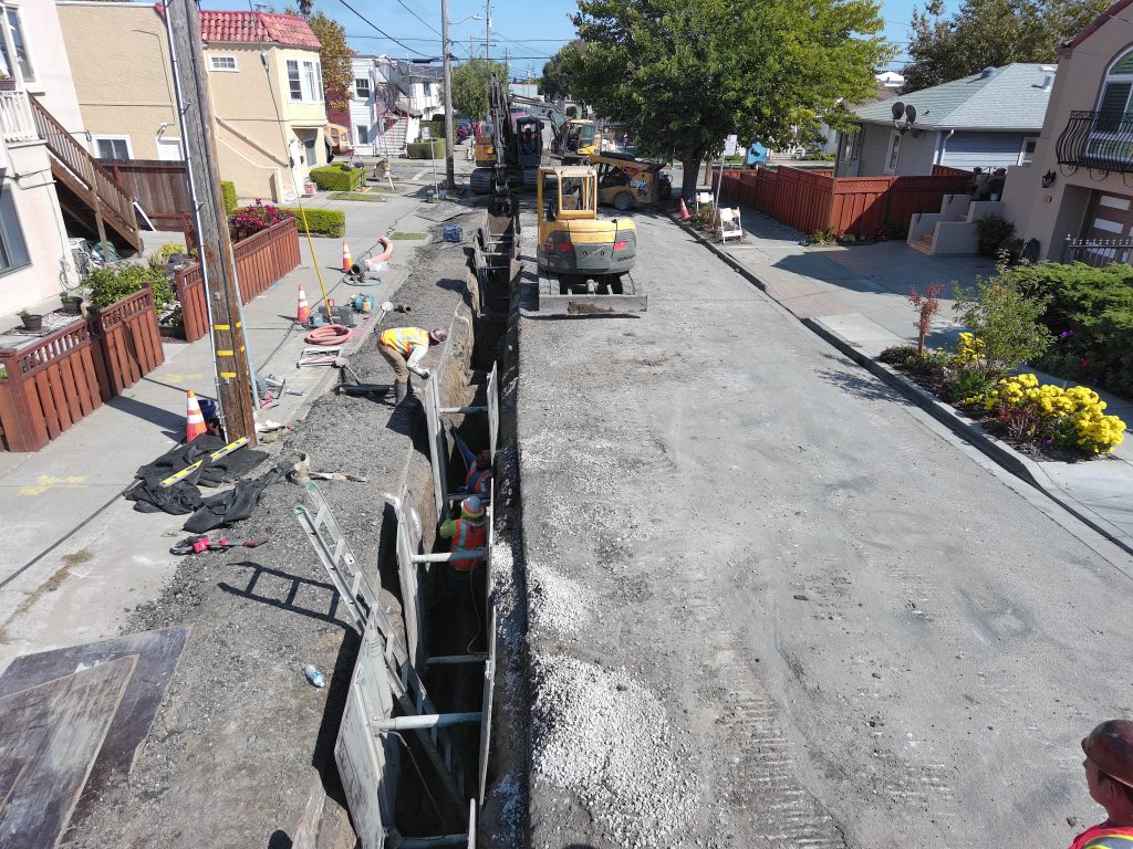 Construction workers installing sanitary sewer pipe in San Bruno street trench.